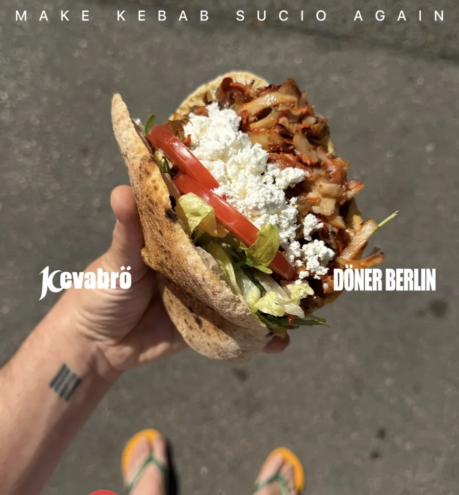 Dürüm abierto con carne, tomate y feta en la mano, sobre el asfalto